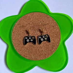May include: A pair of gold-tone earrings shaped like a black video game controller. The controller has white buttons and green and red accents.