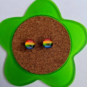 Puede incluir: Un par de pendientes de orgullo arcoíris con el texto "Love is Love" en cada pendiente.
