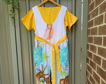 May include: A white jumpsuit with a yellow belt and a blue and white print of birds. The jumpsuit has a yellow sleeveless top attached to the bodice.