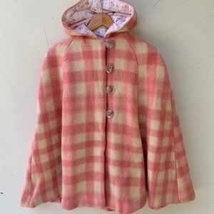 May include: Pink and white plaid hooded cape with decorative buttons. The hood is lined with a floral print fabric.