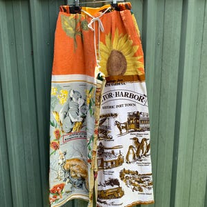 May include: A pair of long, wide-leg trousers made from repurposed fabric. The fabric features a variety of Australian-themed prints, including kangaroos, koalas, and sunflowers. The trousers have a drawstring waist and are a unique and stylish piece of clothing.