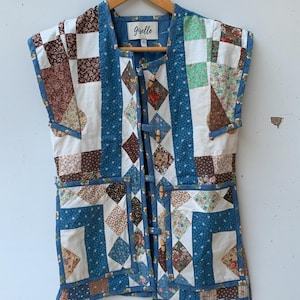 May include: A blue and white patchwork vest with a floral print. The vest has a wooden button closure and a label that says "Giselle".
