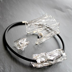 May include: A set of three clear glass necklaces with a black rubber band. The necklaces are made of irregular, textured pieces of glass.