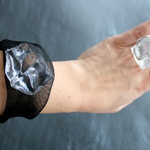 Op de afbeelding: Een zwarte mesh armband met een helder, facetgeslepen kristal in het midden.