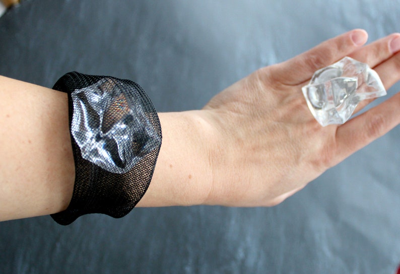 Op de afbeelding: Een zwarte mesh armband met een helder, facetgeslepen kristal in het midden.