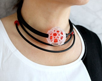 May include: A black choker necklace with three layers of black elastic and a large, clear glass pendant with red accents. The pendant has a bubble-like texture.