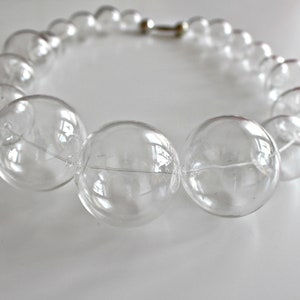 May include: A clear glass necklace with large, round beads. The beads are connected by a thin silver chain.