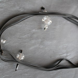 Könnte beinhalten: Eine schwarze Gummikette mit vier durchsichtigen Glaskugeln. Die Kugeln sind mit silbernen Metallringen an der Kette befestigt.