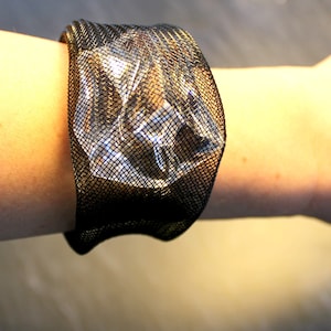 Op de afbeelding: Een zwarte mesh armband met een transparante kunststof inzet. De armband wordt om de pols gedragen.