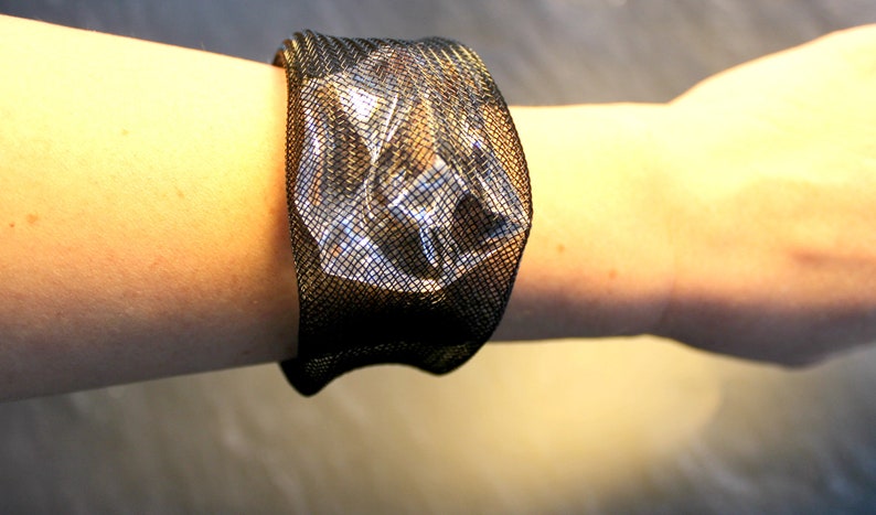 Op de afbeelding: Een zwarte mesh armband met een transparante kunststof inzet. De armband wordt om de pols gedragen.