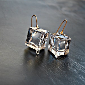 May include: A pair of clear glass earrings shaped like ice cubes with gold-coloured hooks.