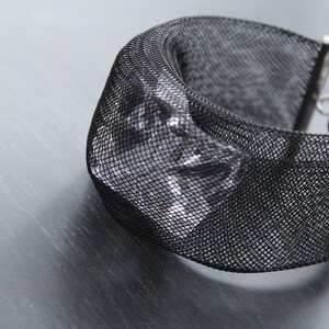 Op de afbeelding: Een zwarte mesh armband met een helder kristal accent. De armband heeft een zilveren sluiting.