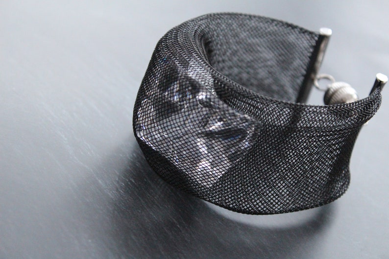 Op de afbeelding: Een zwarte mesh armband met een helder kristal accent. De armband heeft een zilveren sluiting.