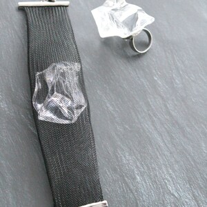 Op de afbeelding: Een zwarte mesh armband met een zilveren sluiting en een ring met een helder kristal en een zilveren band.