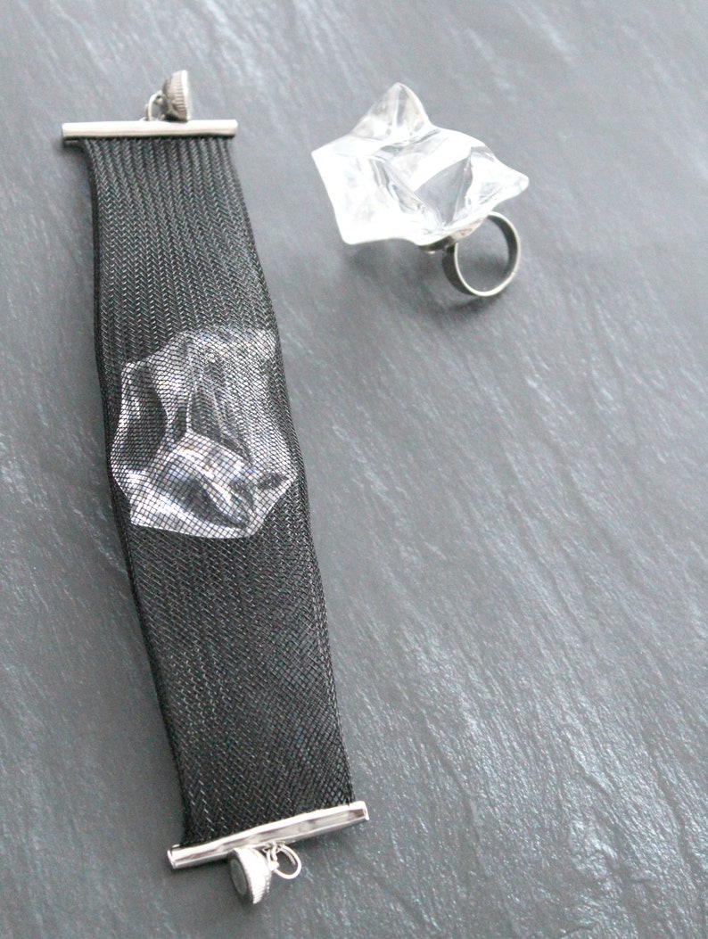Op de afbeelding: Een zwarte mesh armband met een zilveren sluiting en een ring met een helder kristal en een zilveren band.