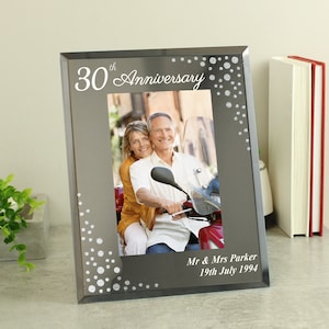 May include: A silver-coloured glass photo frame with a black background. The frame has a white inscription that reads "30th Anniversary" and a photo of a couple on a scooter. The inscription also includes the text "Mr. & Mrs. Parker 19th July 1994".