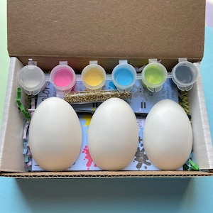 May include: A craft kit for decorating Easter eggs. The kit includes three white ceramic eggs, six small paint pots in pink, yellow, blue, green, and black, and a container of gold glitter.