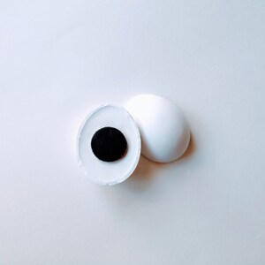 May include: A white ceramic sphere with a black circle in the center. The sphere is split in half, revealing the black circle.