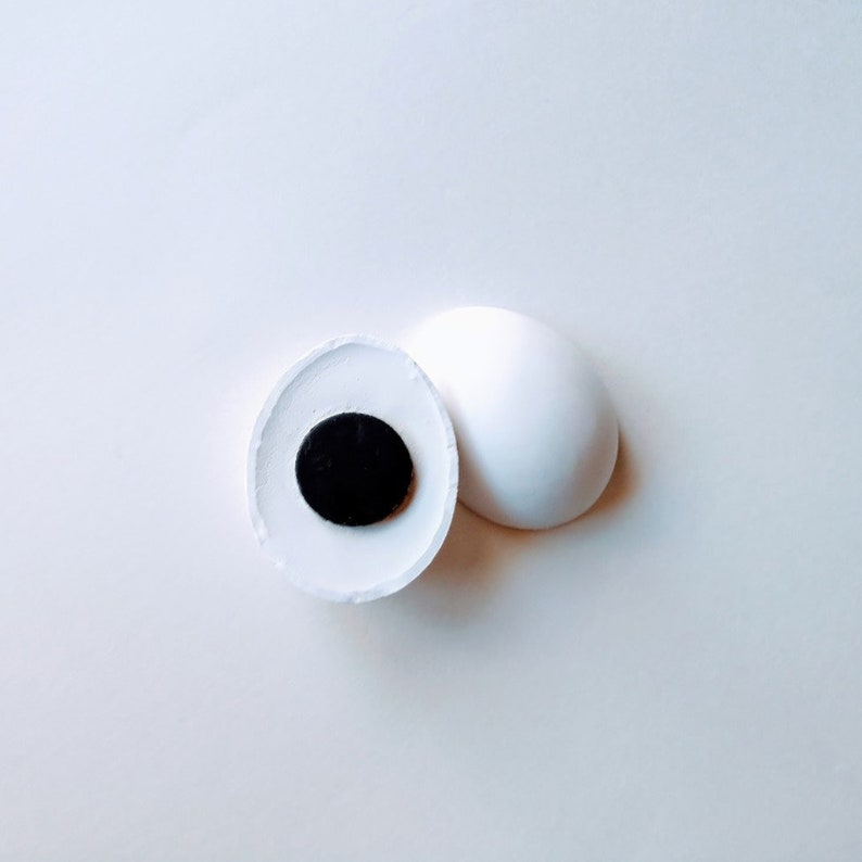 May include: A white ceramic sphere with a black circle in the center. The sphere is split in half, revealing the black circle.