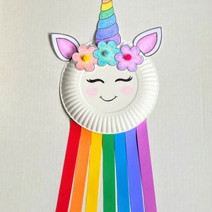 Example of finished unicorn paper plate craft. A face is drawn on a paper plate and a unicorn horn and ears glued on with flowers. Strips of colored paper hang from the bottom in a rainbow.