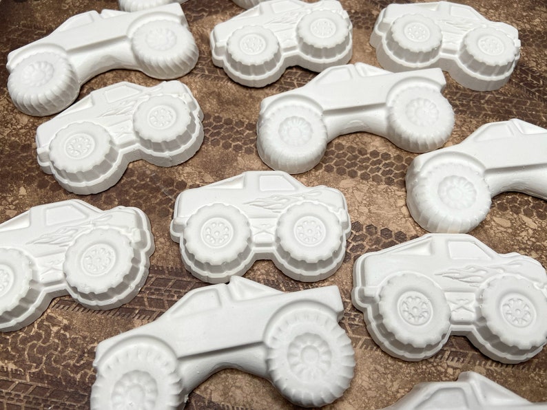 Group of plaster paint your own monster truck magnets. One truck has flames on side and one truck has big wheels and is a longer body.