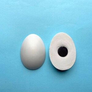 May include: Two white ceramic eggs, one whole and one with a black circle cut out of the center.