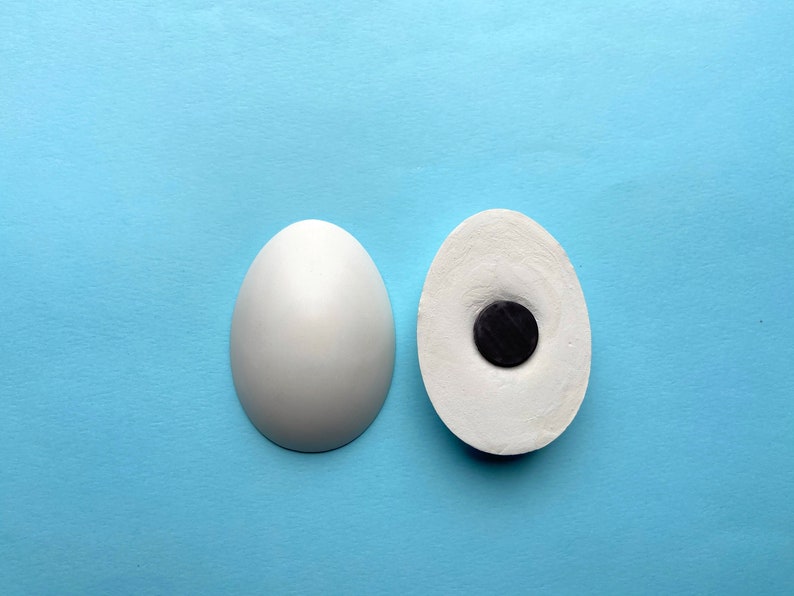 May include: Two white ceramic eggs, one whole and one with a black circle cut out of the center.