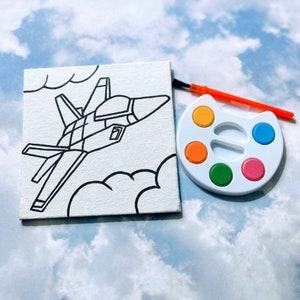 May include: A white canvas with a black line drawing of a jet plane flying through clouds. A white paint palette with six colorful paint wells and a small orange paintbrush are included.