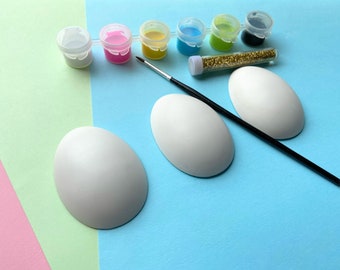 Puede incluir: Un kit de manualidades para decorar huevos de cerámica. El kit incluye tres huevos de cerámica blancos, un pincel, seis pequeños frascos de pintura de varios colores y un frasco de purpurina.