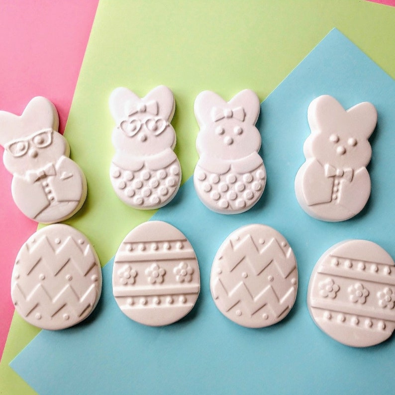 May include: Eight white ceramic Easter egg ornaments with different designs.  The designs include polka dots, zigzags, stripes, and flowers.  Two of the ornaments are shaped like bunnies wearing glasses and bow ties.