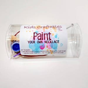 May include: A clear plastic tube containing a paint your own necklace craft kit. The kit includes a wooden necklace, wooden beads, paint pots, and a paint brush. The label reads "Kids Craftables Paint Your Own Necklace".