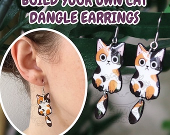 May include: Build your own cat dangle earrings. The earrings feature a calico cat design with orange, black, and white colors. The cat is sitting with its tail dangling down.