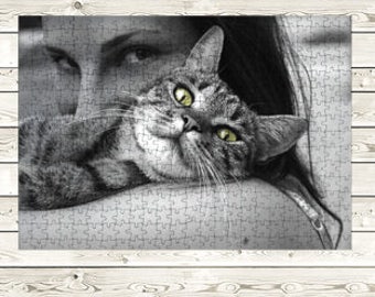 Pode incluir: Uma fotografia a preto e branco de uma mulher com um gato tigrado a descansar no seu ombro. O gato tem olhos verdes e está a olhar diretamente para a câmara.
