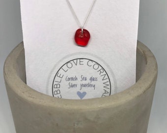 May include: A red sea glass pendant necklace on a silver chain. The necklace is displayed on a white card with the text "Pebble Love Cornwall, Cornish Sea glass, Silver jewellery".