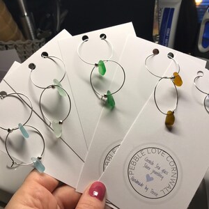 May include: Four pairs of silver hoop earrings with different coloured sea glass accents. The earrings are displayed on white cards with the text "Pebble Love Cornwall, Cornish Sea Glass Silver Jewellery, Handmade by Terri".