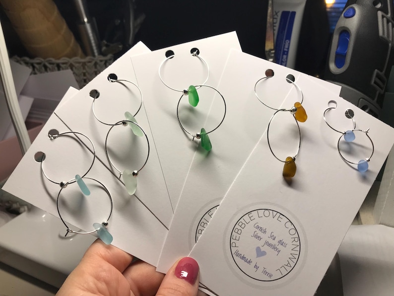 May include: Four pairs of silver hoop earrings with different coloured sea glass accents. The earrings are displayed on white cards with the text "Pebble Love Cornwall, Cornish Sea Glass Silver Jewellery, Handmade by Terri".