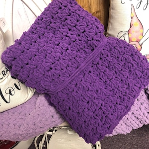 May include: A purple crocheted throw pillow with a textured, chunky knit pattern. The pillow is soft and fluffy, and would be a great addition to any living room or bedroom.