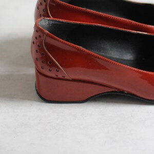 May include: A pair of red patent leather shoes with a wedge heel and a perforated design.