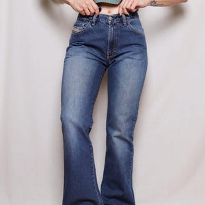 May include: Blue denim flared jeans. The jeans have a classic five-pocket design, a zip fly, and a button closure. The jeans have a faded wash and a flared leg opening. The jeans are a vintage style.
