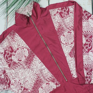 May include: A burgundy zip-up jacket with a white geometric pattern. The jacket has a drawstring at the bottom and a zipper closure.