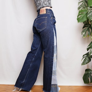May include: Dark wash denim jeans with a wide leg and a patchwork design down the side. The jeans have a classic five-pocket design and a frayed hem. The patchwork features various shades of blue denim with decorative stitching.