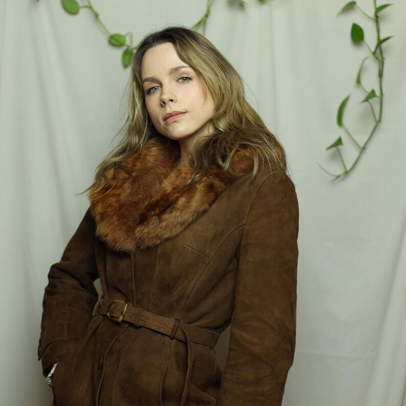 May include: A brown suede coat with a faux fur collar and a belt. The coat has a classic design with a belted waist and a warm, inviting appearance. The coat is a stylish outerwear option.