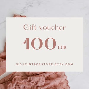 Puede incluir: Un vale de regalo con el texto "Gift voucher" y "100 EUR" en un color suave y apagado. La URL de la tienda de Etsy se muestra en la parte inferior. El vale está sobre un fondo de tela rosa.