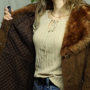 May include: Brown suede coat with a faux fur collar and quilted lining. The coat has large buttons and a classic design. The interior lining is a dark brown color. The coat is open, revealing the interior.