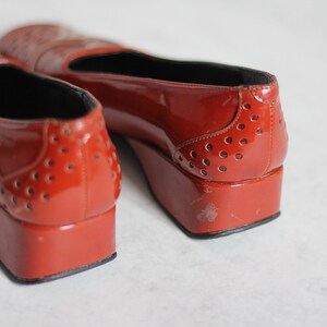May include: A pair of red patent leather shoes with a platform heel and a perforated design. The shoes have a pointed toe and a black lining.