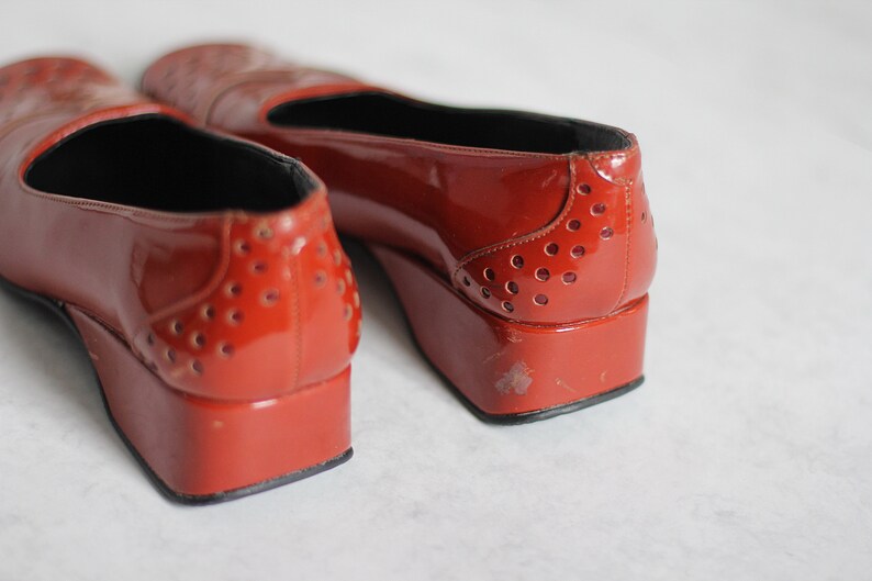 May include: A pair of red patent leather shoes with a platform heel and a perforated design. The shoes have a pointed toe and a black lining.