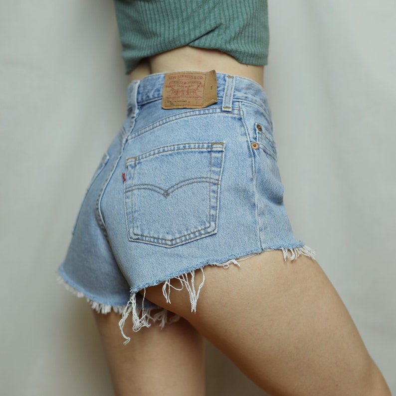 Puede incluir: Pantalones cortos de mezclilla azul claro con bordes deshilachados y un parche de cuero marr&oacute;n Levi's en el bolsillo trasero.