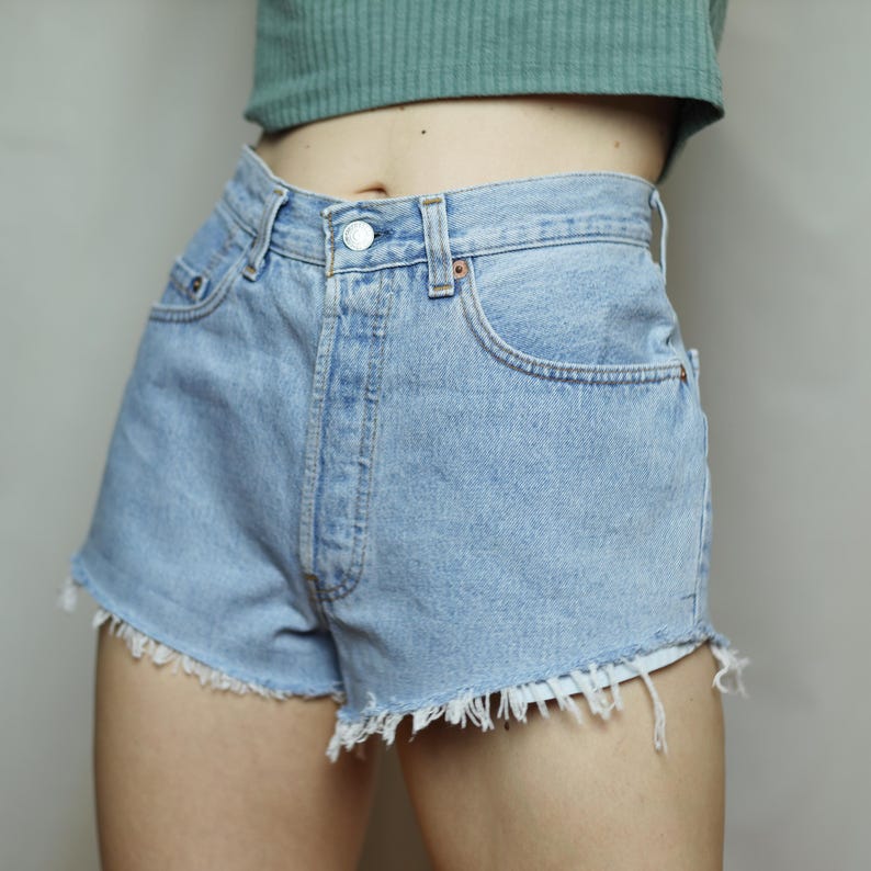 Puede incluir: Pantalones cortos de mezclilla azul claro con dobladillo deshilachado. Los pantalones cortos tienen cintura alta y cierre de bot&oacute;n.