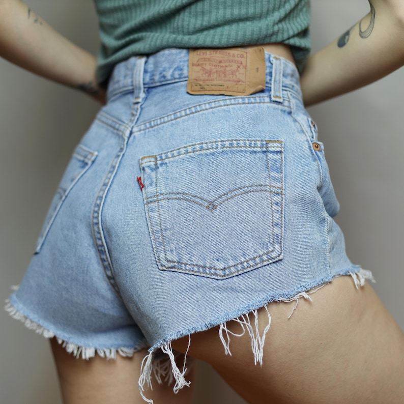 Puede incluir: Pantalones cortos de mezclilla azul claro con dobladillo deshilachado y un bolsillo trasero con una etiqueta roja que dice "Levi's".