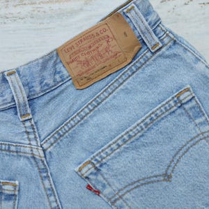 Puede incluir: Un par de pantalones vaqueros de mezclilla azul claro con un parche de cuero marr&oacute;n Levi Strauss & Co. en el bolsillo trasero. El parche tiene el texto "Levi Strauss & Co." y "Quality Clothing" impreso en &eacute;l. Los pantalones tienen un bolsillo trasero con una leng&uuml;eta roja que dice "Levi's".